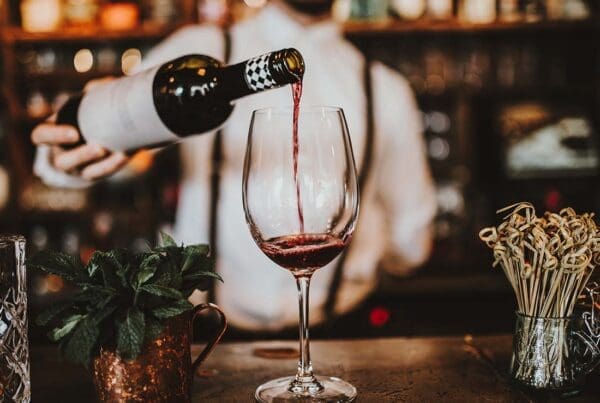 Liquor Liability Insurance - Close-up View of a Bartender Pouring Red Wine into a Glass over an Antique Bar with Bottles Blurred in the Distance