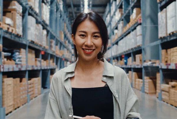 Workers’ Compensation Insurance - Portrait of Young Business Manager Smiling and Looking at Camera While Holding a Tablet and Standing in Retail Distribution Center