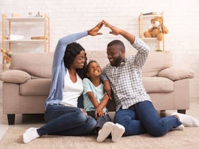 Blog - Cheerful Parents and Young Daughter Sitting in Front of the Sofa in the Living Room Putting Their Hands Up in the Air to Make a Roof Shape