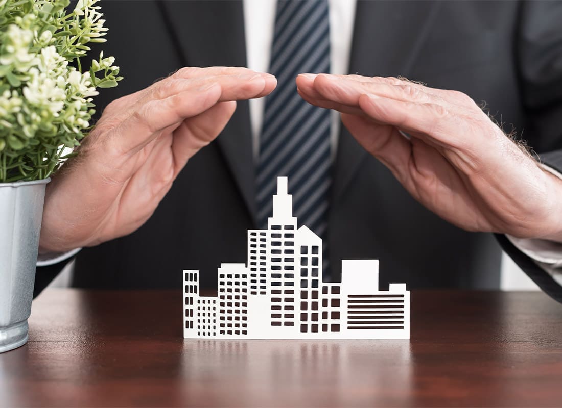 Professional Liability Insurance - Insurance Agenct With Hands Over a Small Paper Cut-out of a City to Represent Business Insurance